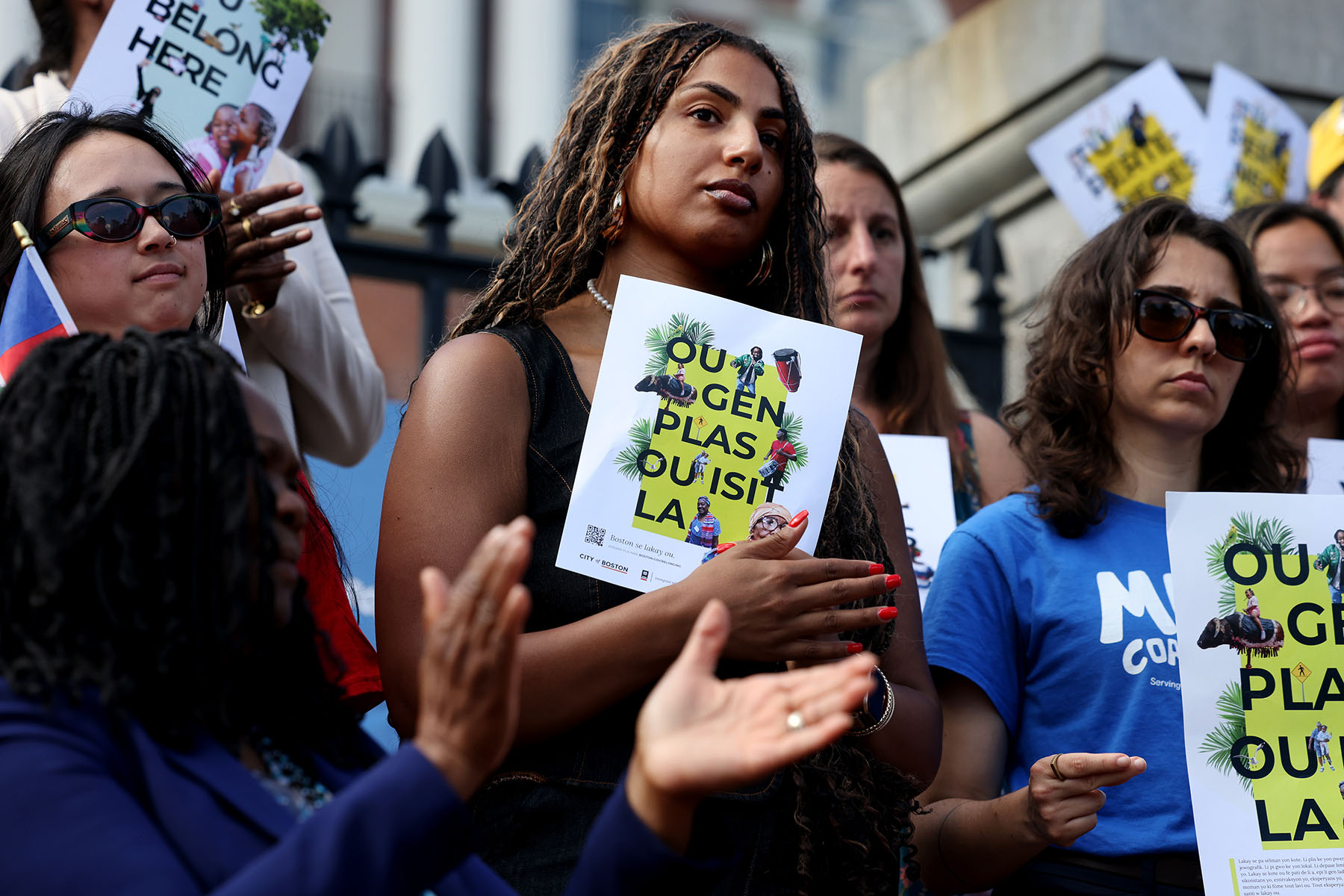 People hold sign of support written in Haitian Creole that translates to "You Belong Here" during a press conference.