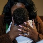 A woman cradles an infant, holding the baby's head with both hands.