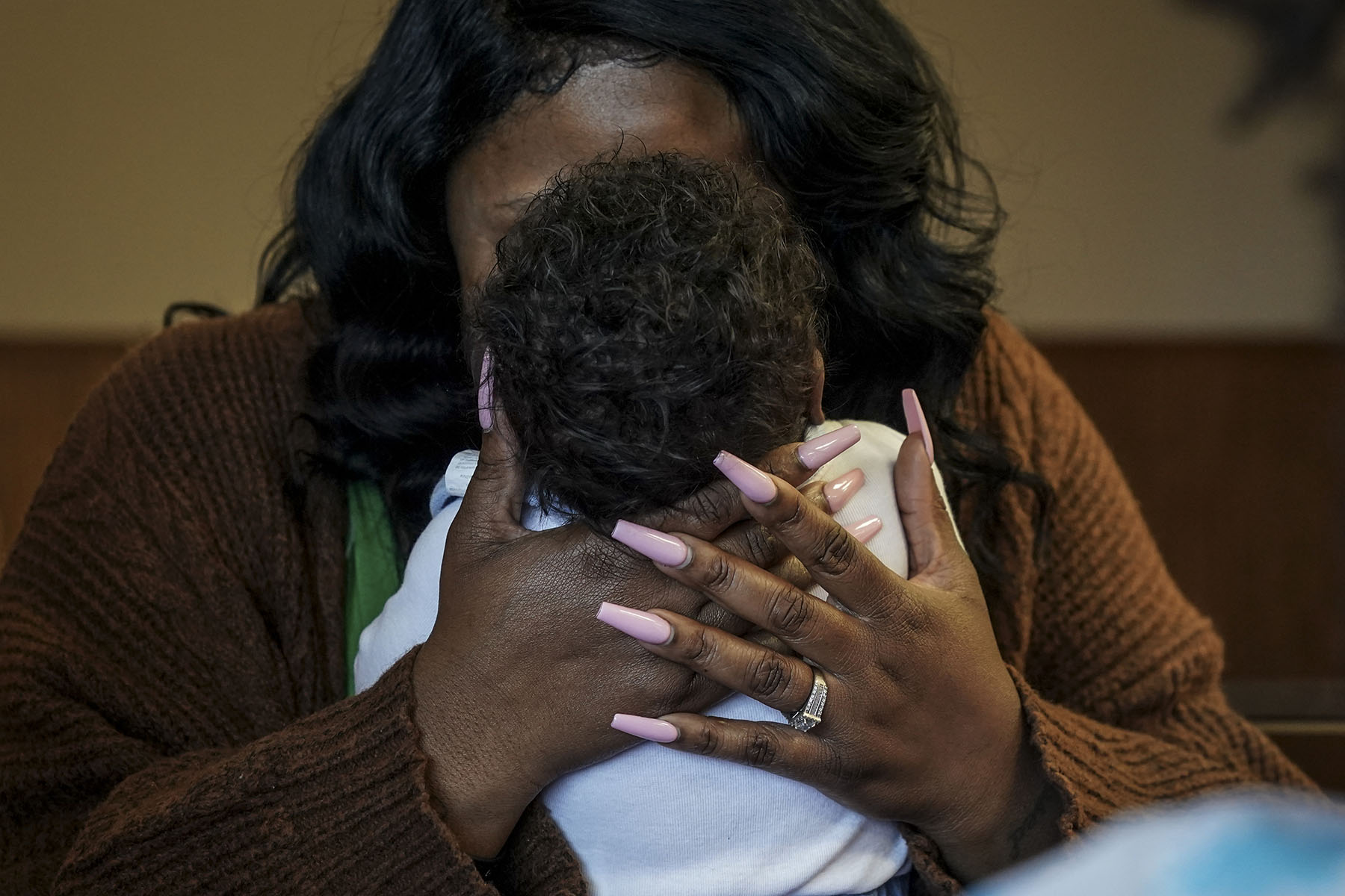 A woman cradles an infant, holding the baby's head with both hands.