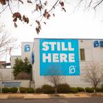 The exterior of a Planned Parenthood building with a banner draped on one wall saying Still Here.