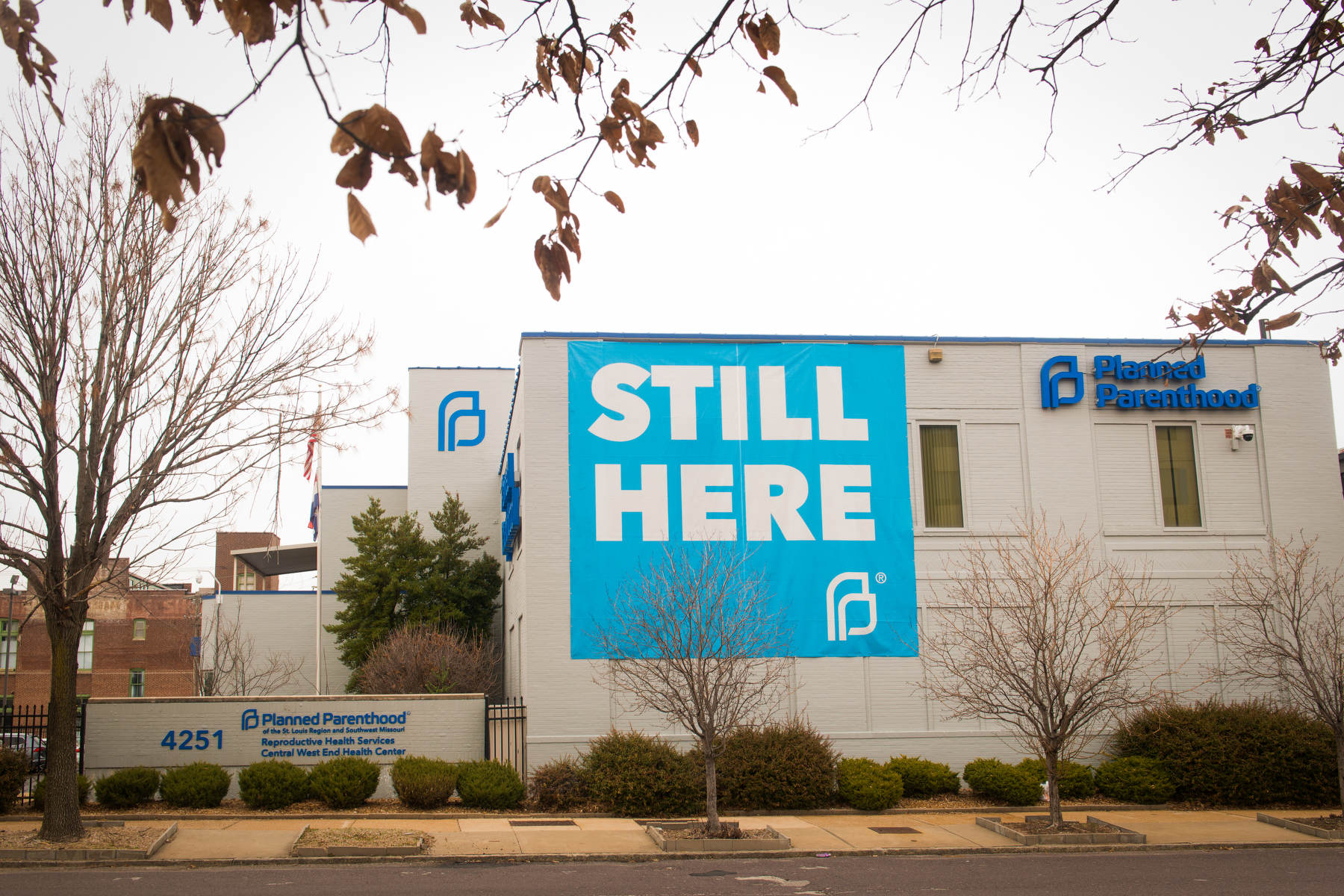 The exterior of a Planned Parenthood building with a banner draped on one wall saying Still Here.