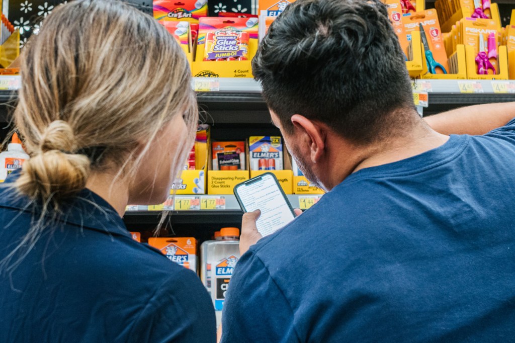 Two people look at a school supply list on a phone while shopping.