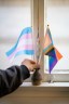 A hand tidies two LGBTQ+ flags sitting in a vase on a windowsill in closeup.