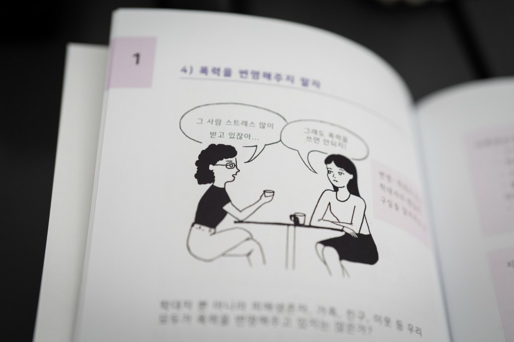 A white booklet with an illustration of two women speaking to each pother seated at a table, surrounded by Korean text.