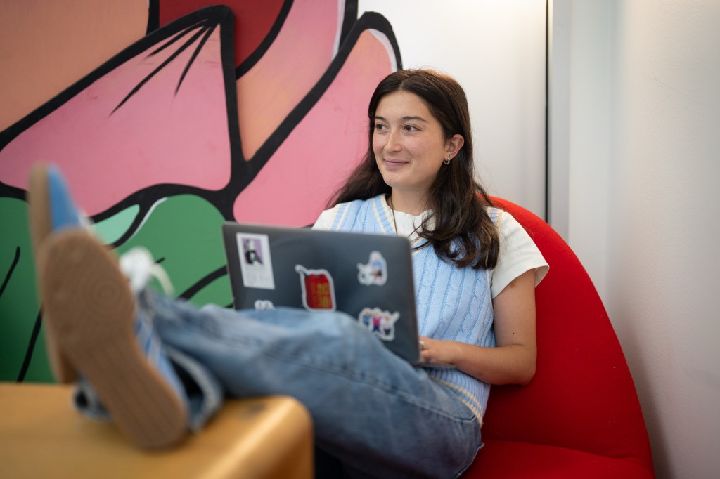 A person sits in a red chair with their feet on a table and a laptop in their lap.
