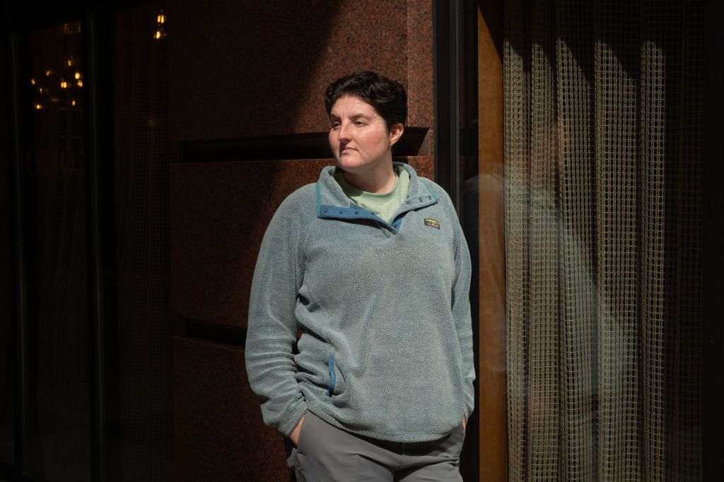 A portrait of a person outside standing against a an exterior wall.