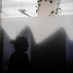 A woman is reflected in silhouette against a window background, maintaining her visual anonymity.