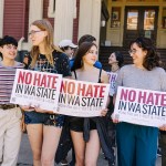 young people walk near each other, each holding signs that read, “No hate in WA state. Vote No on I-001 & I-638.”