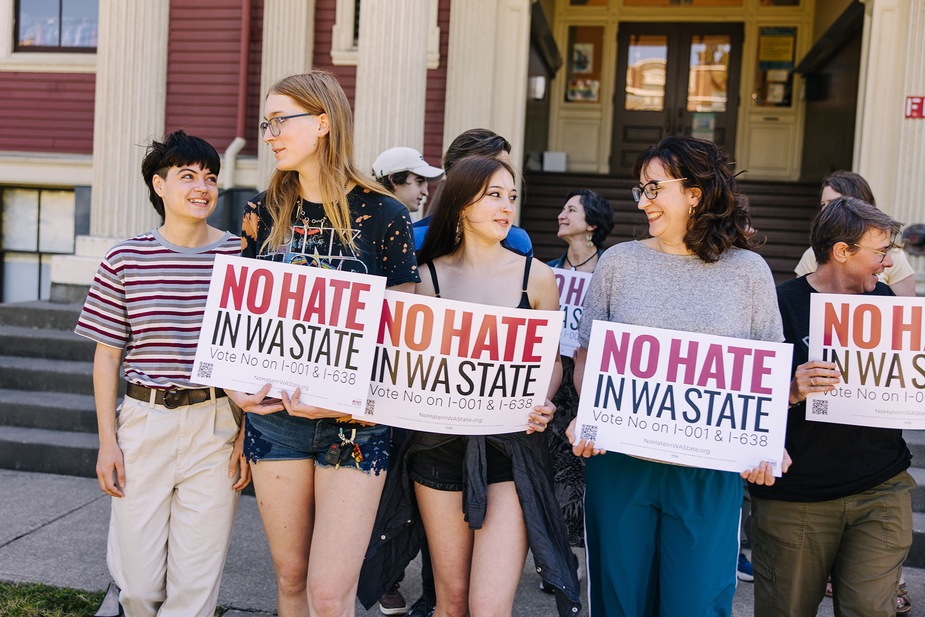 young people walk near each other, each holding signs that read, “No hate in WA state. Vote No on I-001 & I-638.”