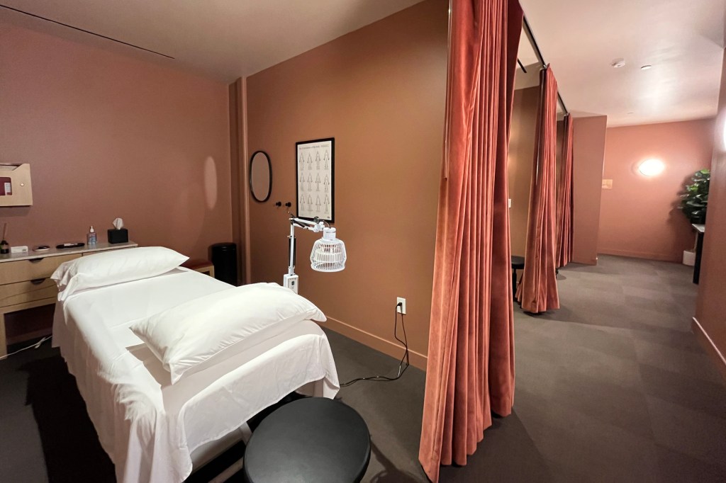 An empty bed sits in an earth-tone room among a suite of medical curtained rooms.