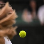 The long hair of a female tennis player obscures the face of another while a tennis ball hovers in midair in front of them.
