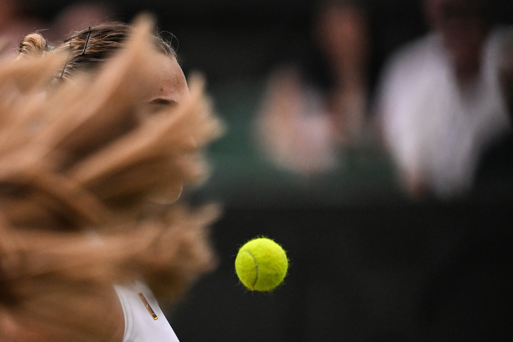 The long hair of a female tennis player obscures the face of another while a tennis ball hovers in midair in front of them.
