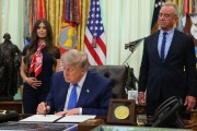 President Donald Trump signs a document with a black pen, with a woman holding her pregnant belly to the left of him and Robert F. Kennedy Jr. to the right.