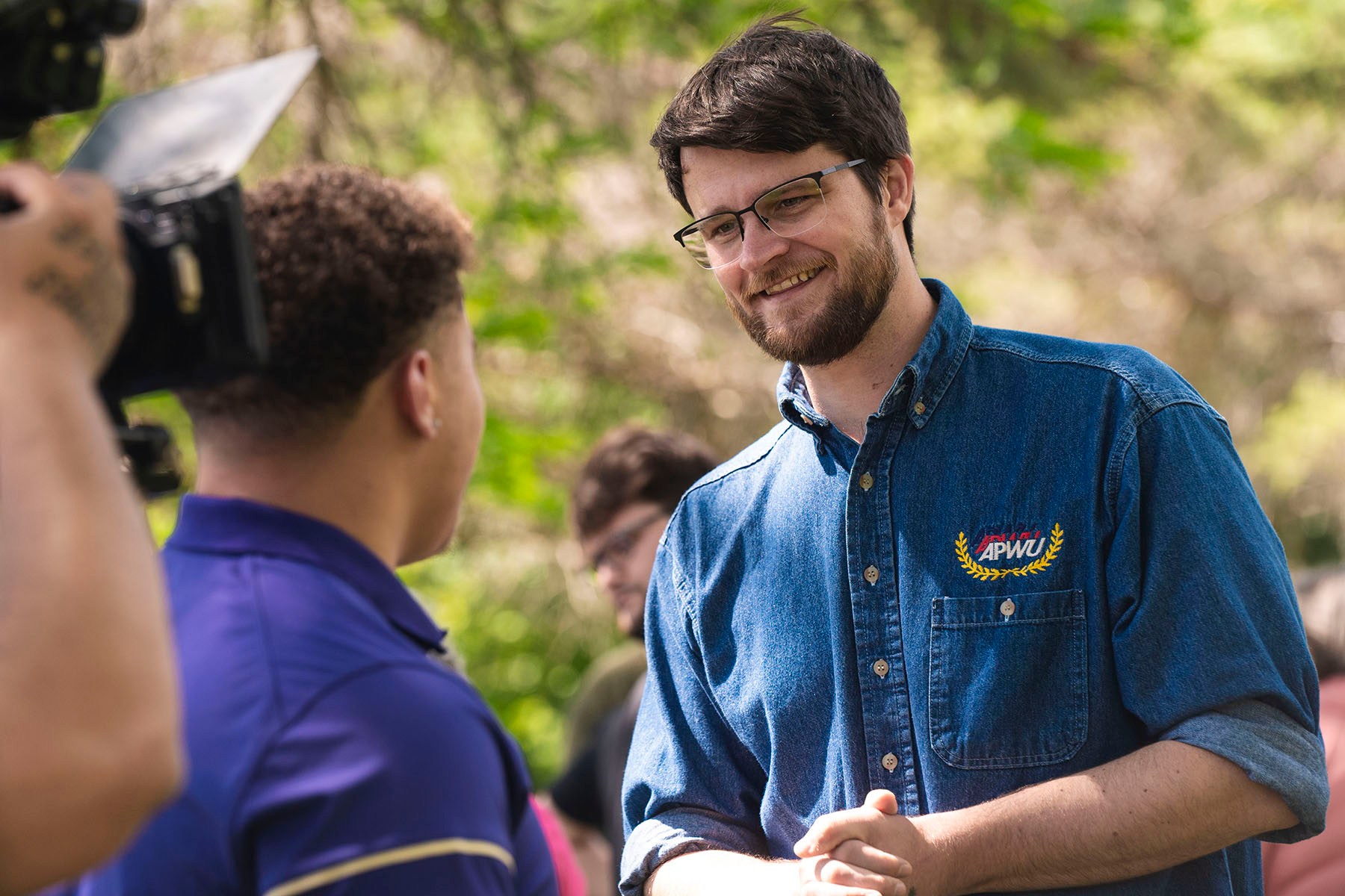 Will Lawrence smiles while speaking with a constituent outdoors.