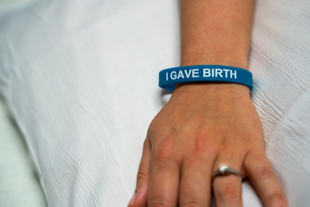 A closeup on a hand wearing the I gave birth wristband.