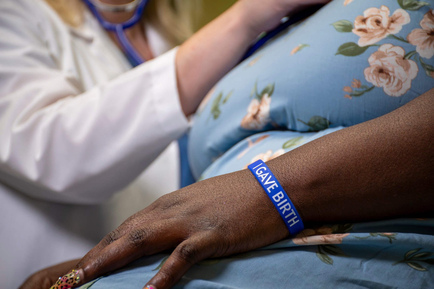 A closeup photo on a woman's wrist wearing the I gave birth wristband, with a nurse checking her vitals in the background.
