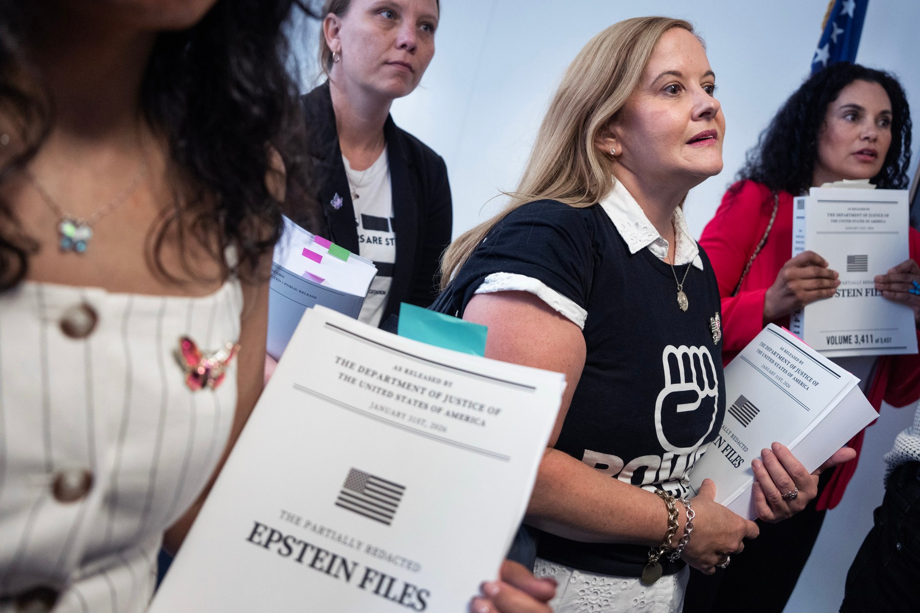 A group of women carry copies of the Epstein files in their hands while standing in a hallway.