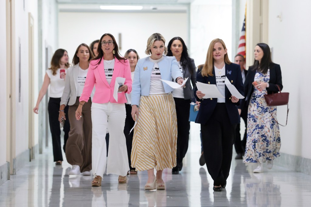 A group of women walk down a hallways together carrying sheets of paper.