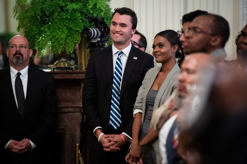 Kirk and Owens stand beside each other smiling in a room full of people.