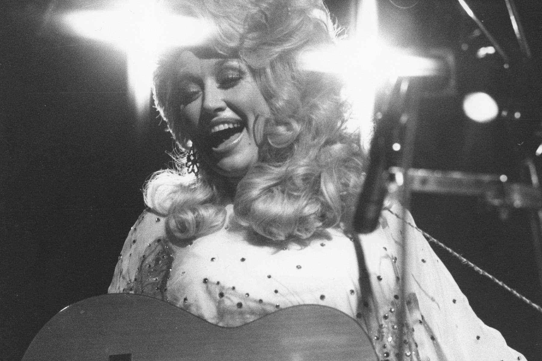 Parton ringed by lights on stage singing and playing guitar.