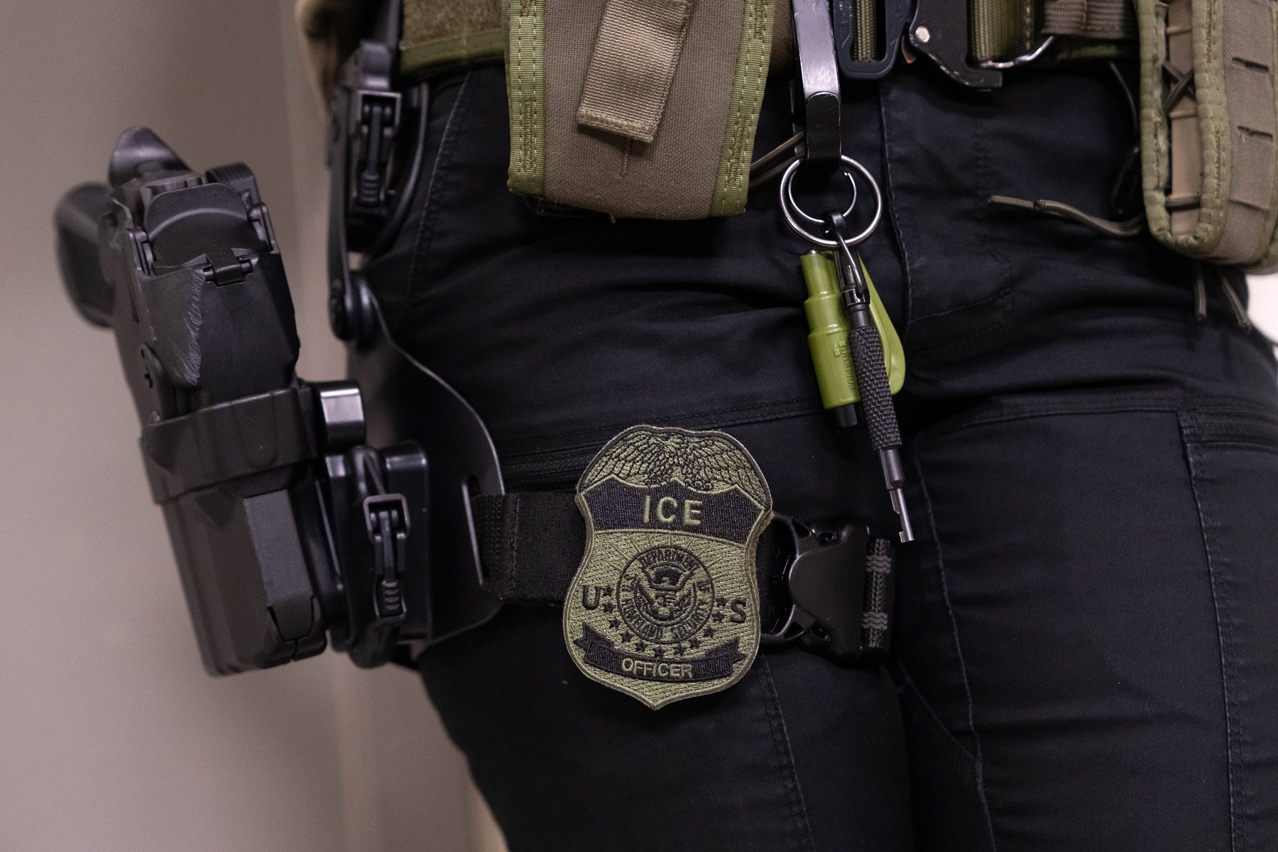 A photo depicts an ICE officer's badge and gun holster.