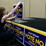 A woman crouches beside a stage, attaching a blue-and-yellow 