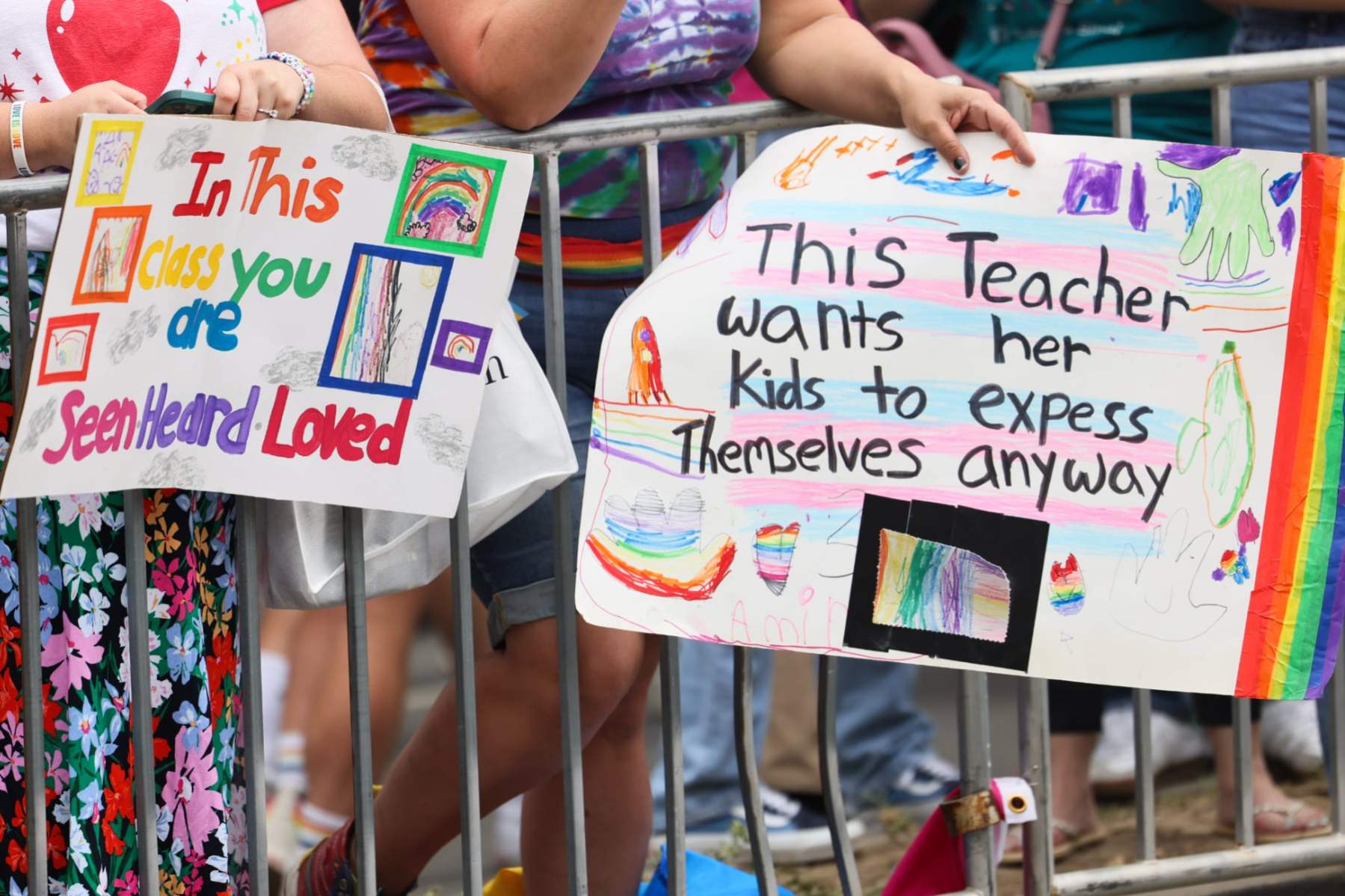 Signs that say "in this class you have seen heard loved" and "This teacher wants her kids to express themselves anyway" are held over a railing.