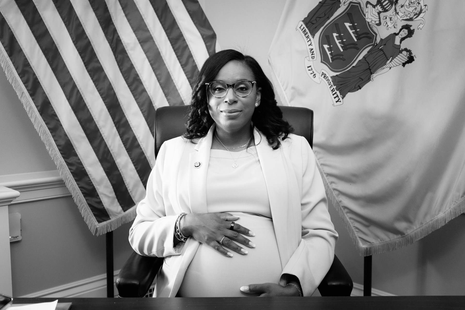 A portrait of McIver in an office surrounded by flags and holding her pregnant belly.