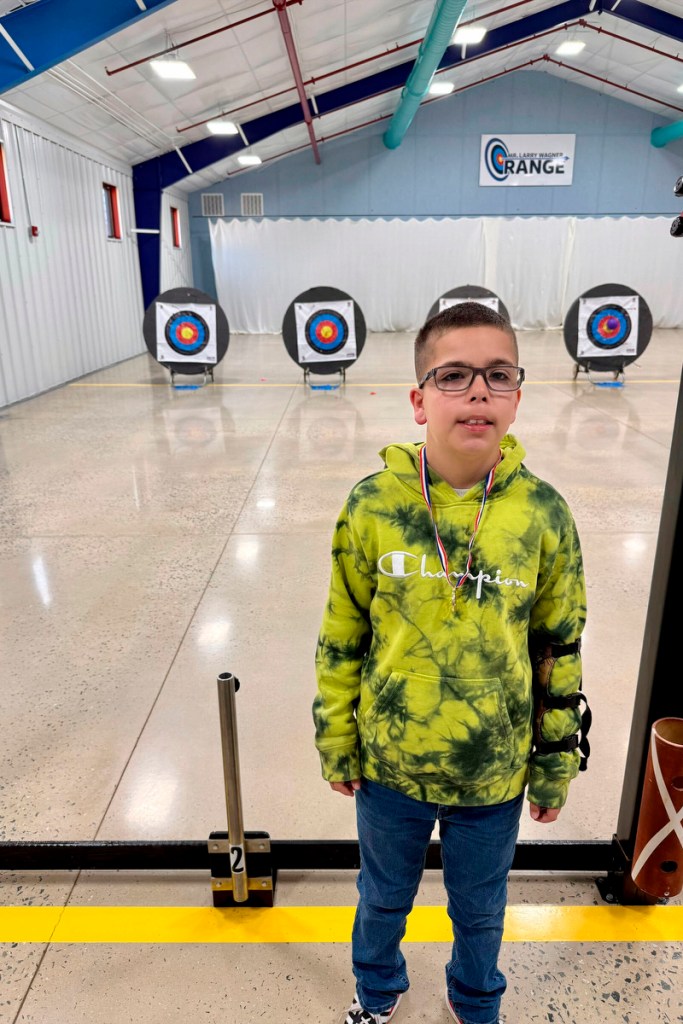 Dylan stands in front of an archery range.