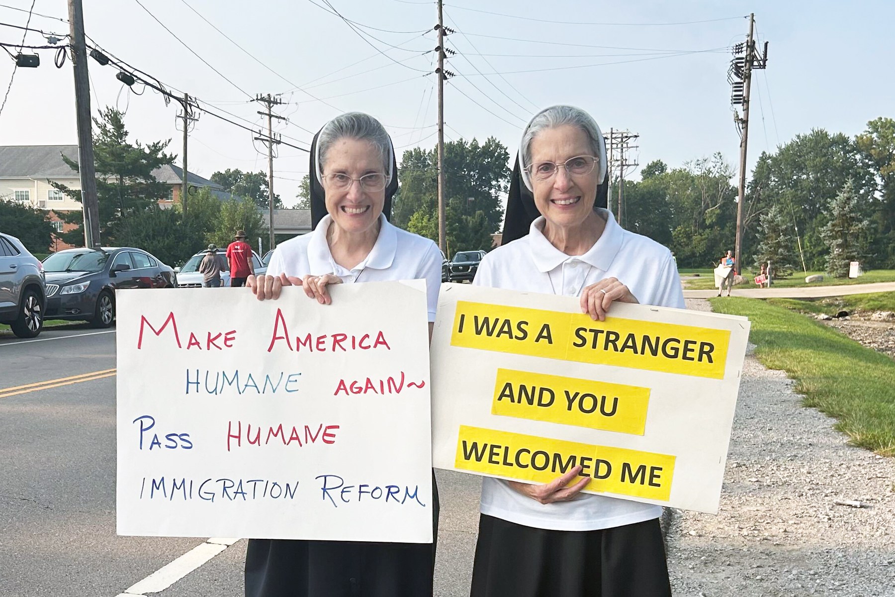 Two Catholic nuns hold signs related to immigration enforcement outside of an ICE facility.