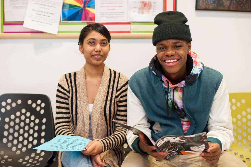Two people smile at the camera while seated.
