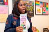 A person holds up a brochure about signs of a healthy relationship in a room with educational materials on the wall behind her.