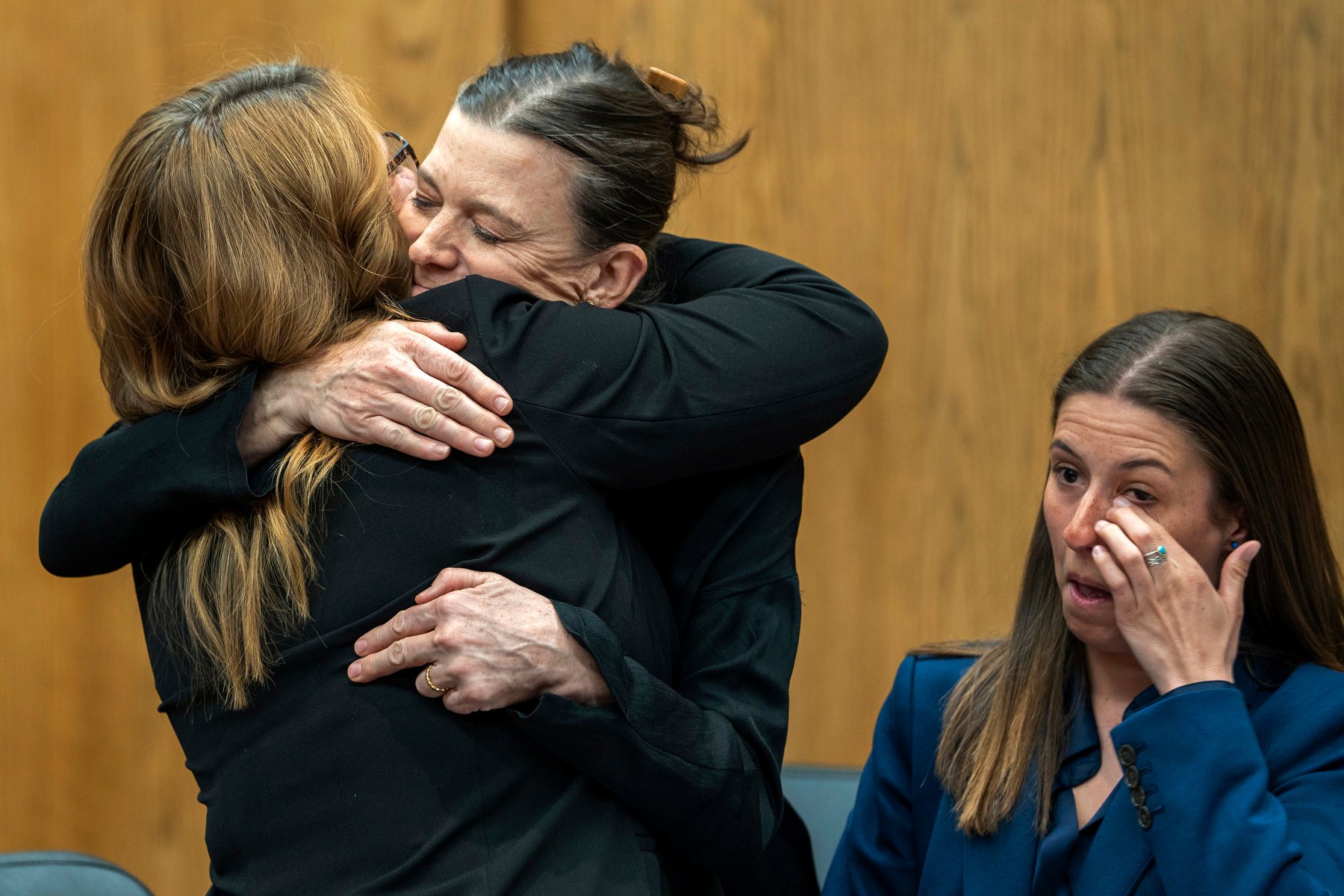 Two women hug while another person sits near them in a courtroom.