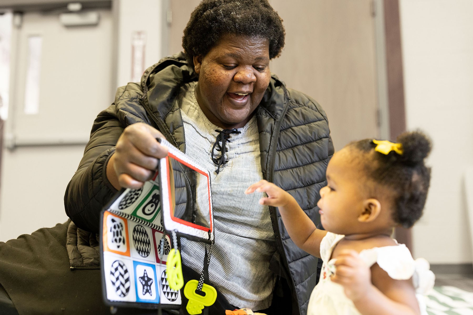 Edythe Smith smiles while holding up a soft activity book as her daughter Judith reaches toward it.
