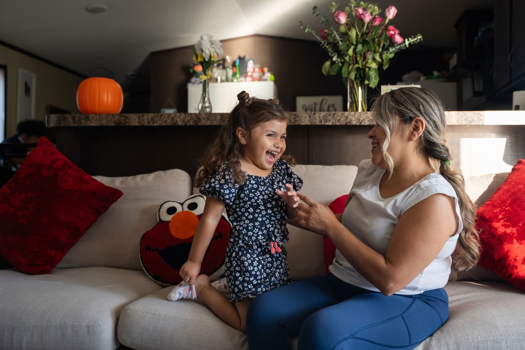 Barbara Aranda smiles at her daughter, Mackenzie, as they play together on a couch at home.