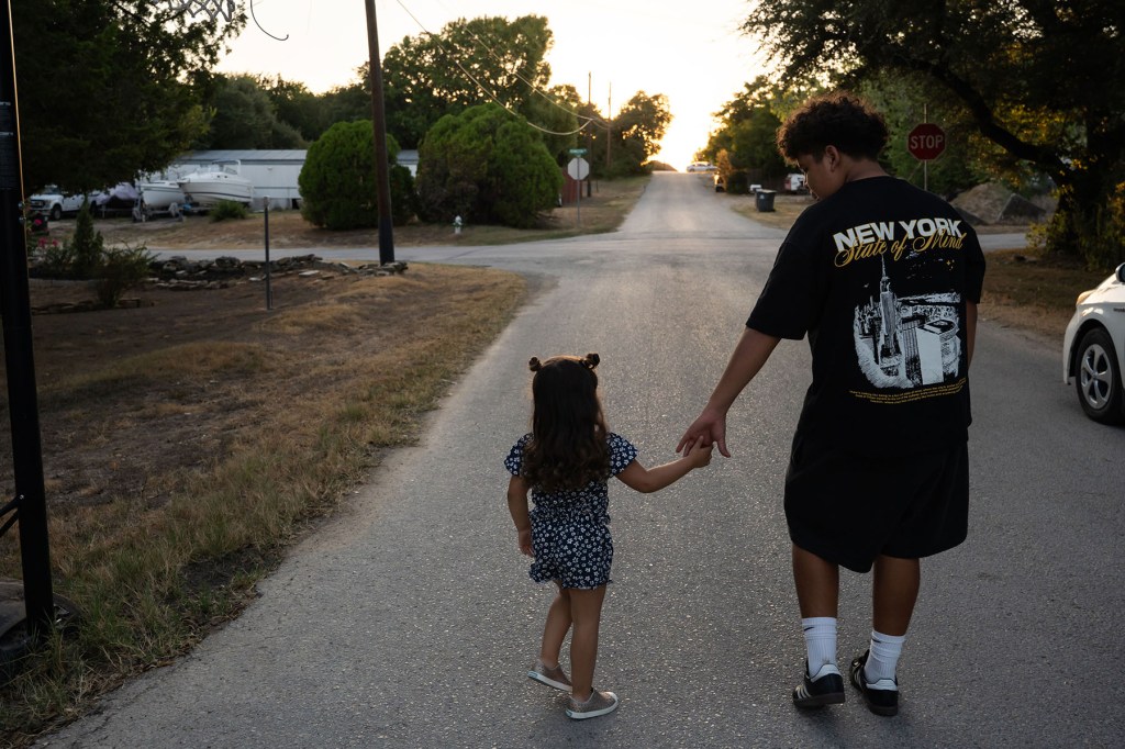 Mackenzie walks hand in hand with her brother, Luke, down a residential street at sunset.