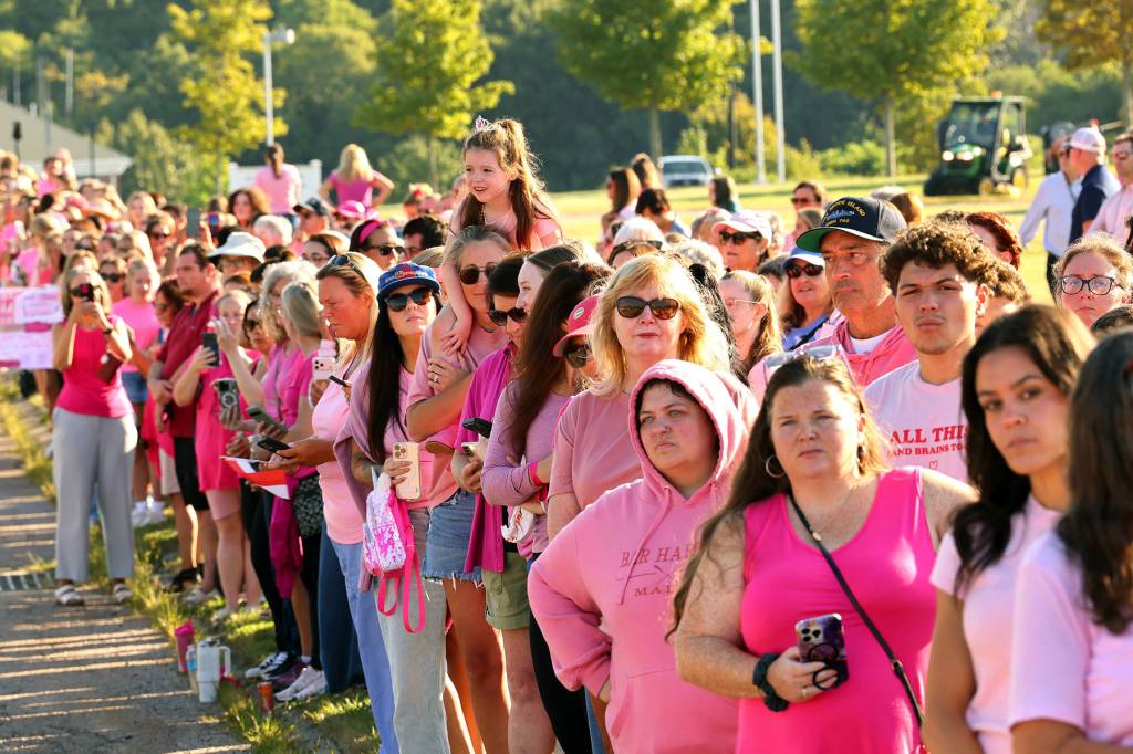 A group of mostly women, wearing varying shades of pink, stand together looking toward something out of frame.