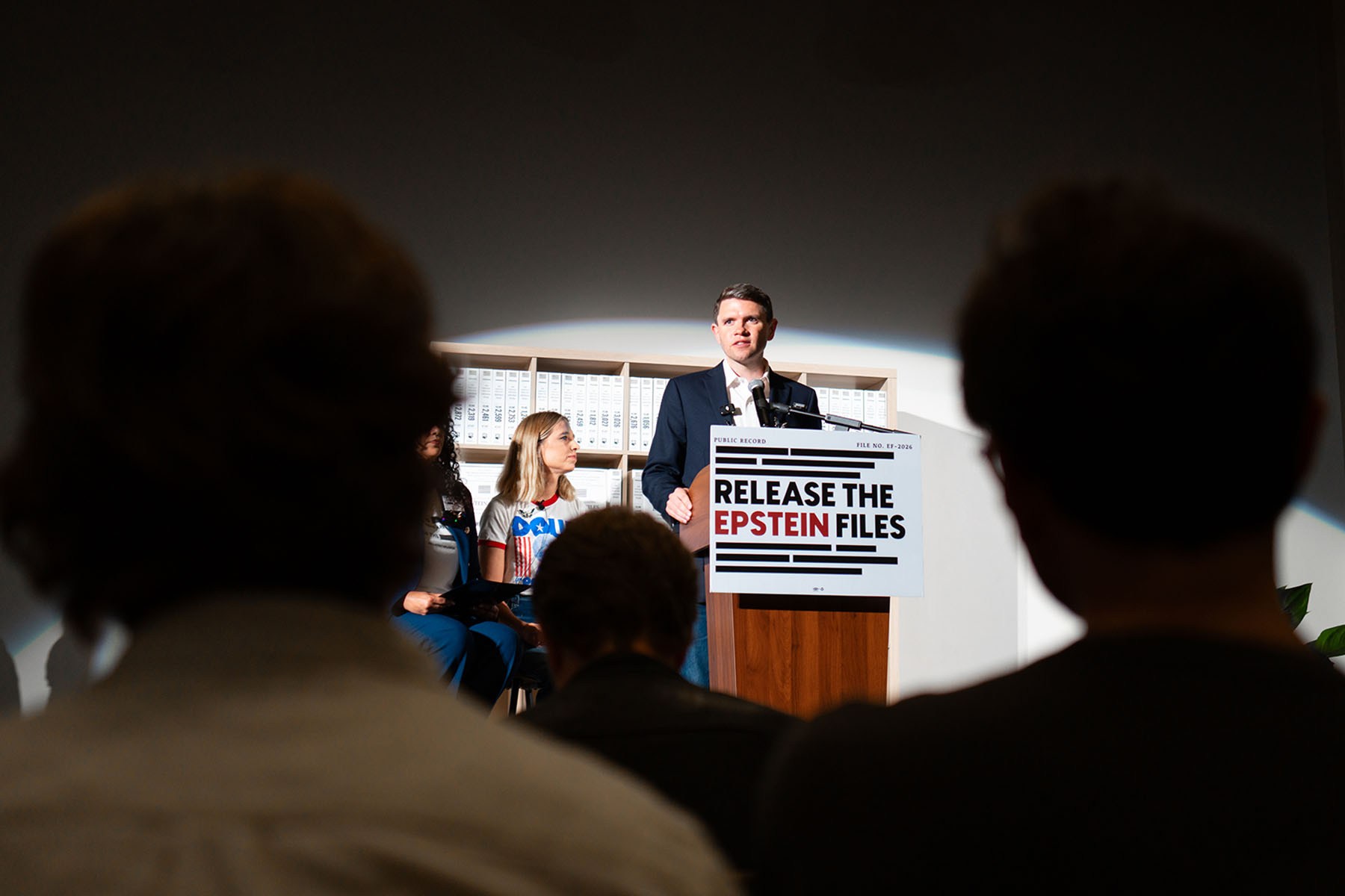 James Talarico speaks at a podium with a sign reading "Release the Epstein Files" as audience members sit in the foreground.