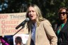 Clayton speaks at a podium with a sign and another woman behind her.
