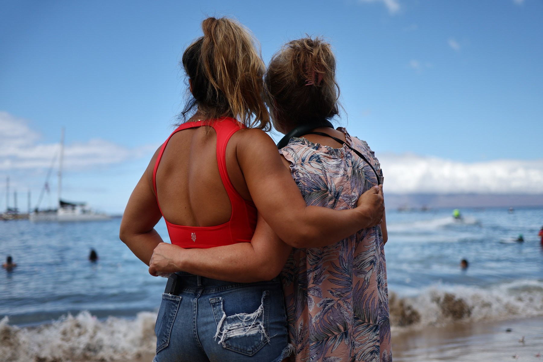 Two women embrace at the edge of the shore in Hawaii.