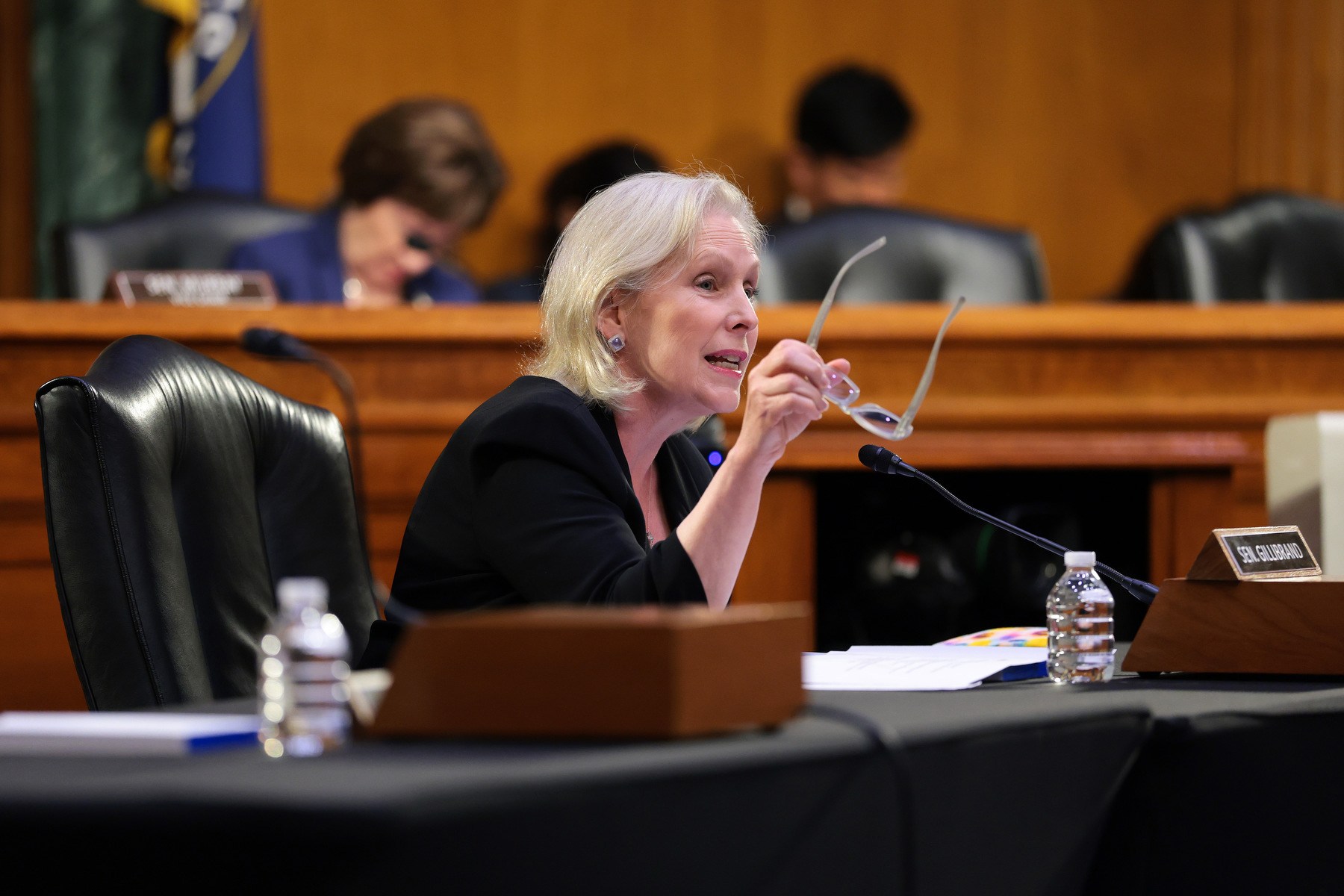 Gillibrand gesticulates with eyeglasses in hand from a chair in Congress.