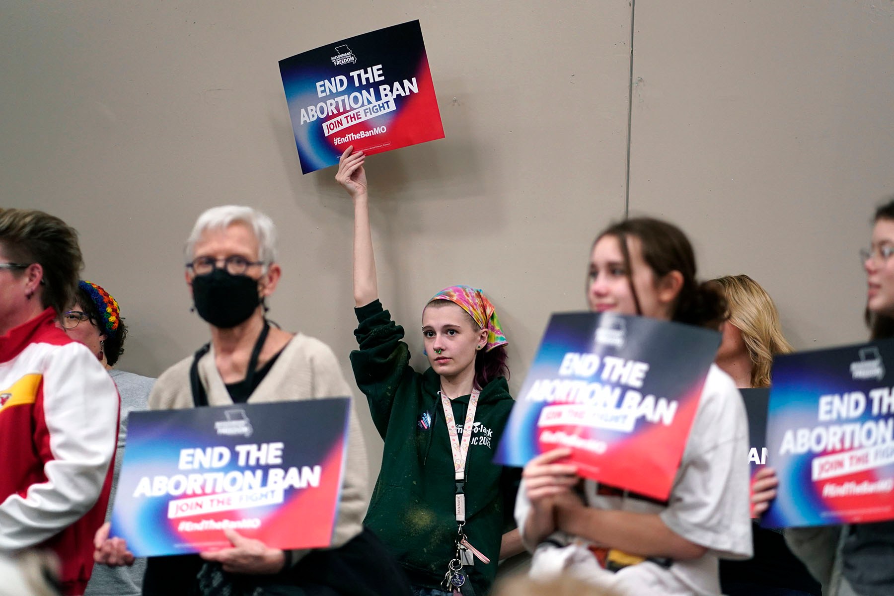 A person holds an "End the Abortion Ban" sign above their head while standing among a crowd of supporters holding matching signs at a Missouri abortion rights event.
