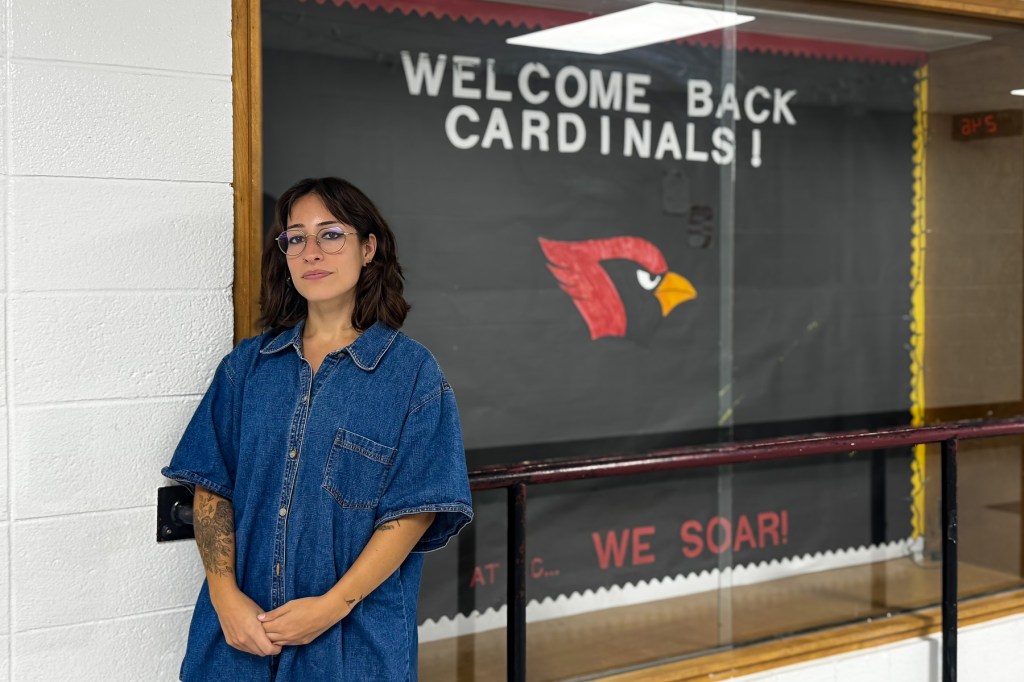 A woman stands with hands clasped in front of a welcome back cardinals sign in a school hallway.