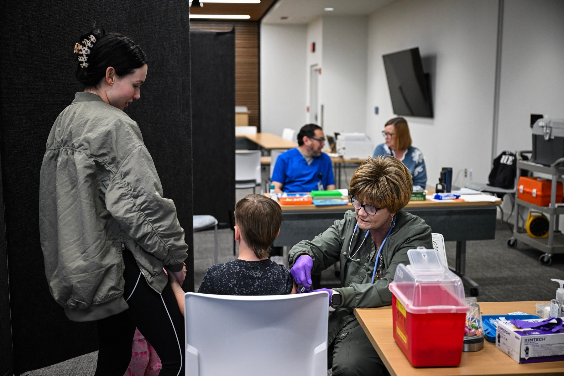 A nurse administers a vaccine to a child while others look on in the room.