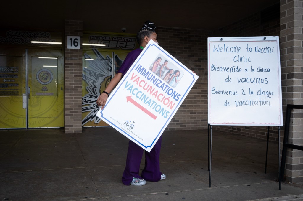 A woman carries a sign advertising an open vaccine clinic at a school.