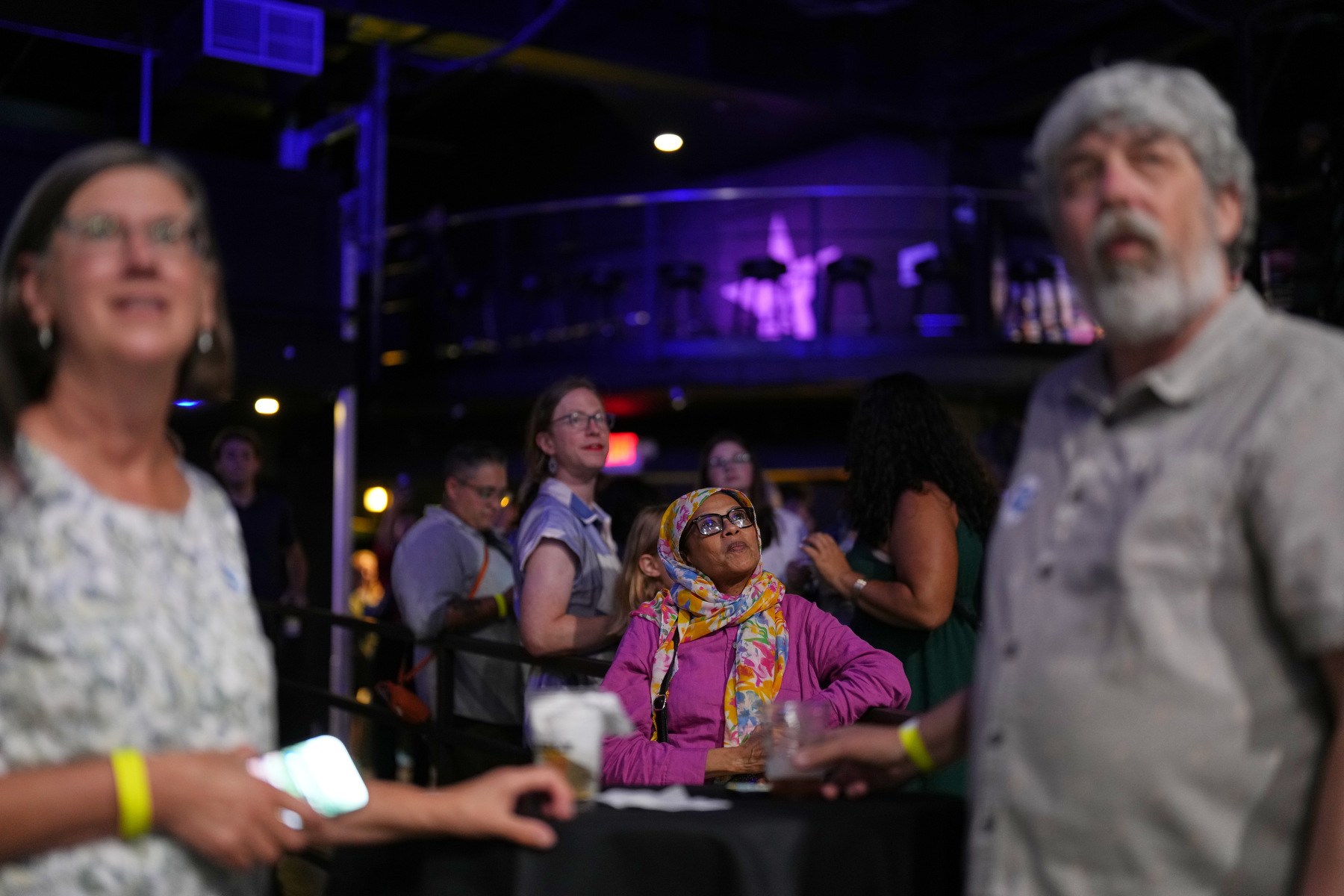 A woman looks up while seated at a table and surrounded by other attendees also looking up at something offscreen.