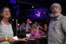 A woman looks up while seated at a table and surrounded by other attendees also looking up at something offscreen.