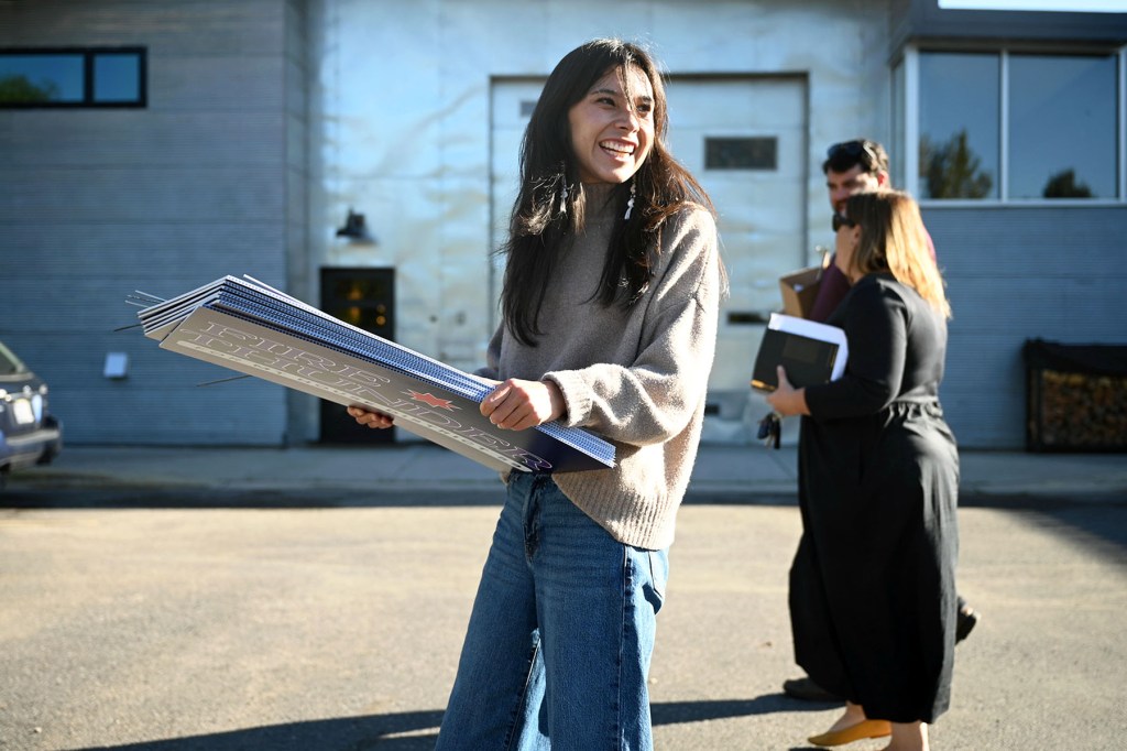 Katie Fire Thunder smiles while carrying a stack of campaign signs outside a building.