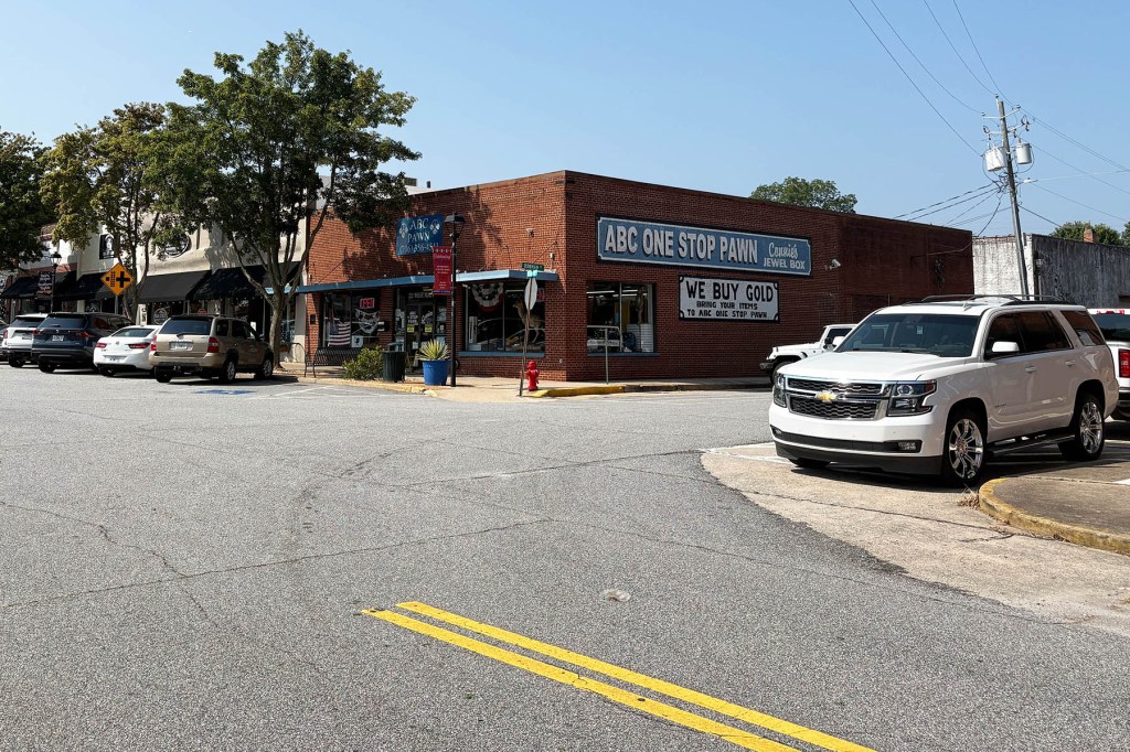 A brick pawn shop sits at a street corner in downtown Lavonia, Georgia, with several parked cars and a white SUV in the foreground.