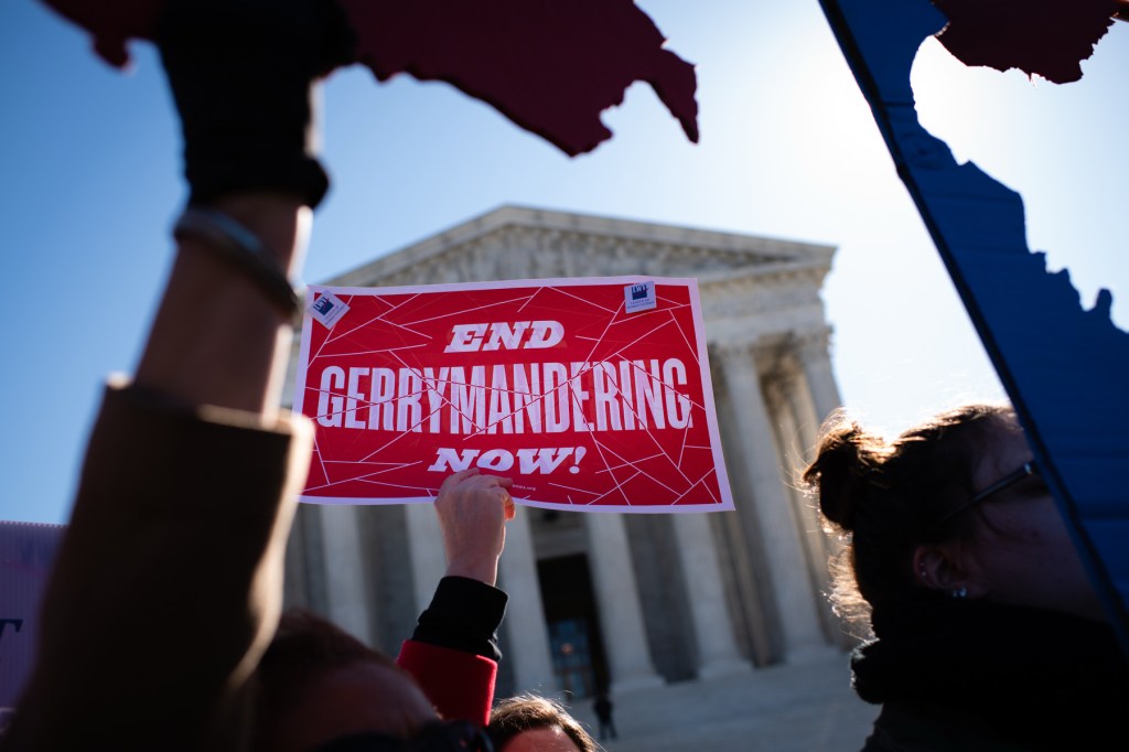 A sign that says end gerrymandering now is held aloft by arms in silhouette against the backdrop of the Supreme Court building.